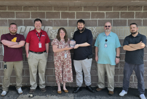 Executive Director Amy Tomlinson presents Dustin Smith with the Employee Excellence Award for April 2026. They are flanked by other members of the IT team.